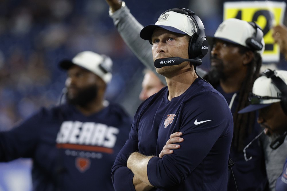 Chicago Bears head coach Ben Johnson, arms crossed and wearing a headset, watches a replay on the video board at Nissan Stadium