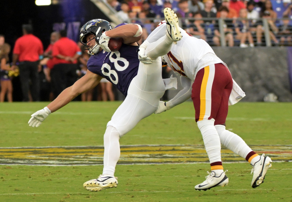 A Ravens tight end in purple is brought down by a Commanders defender