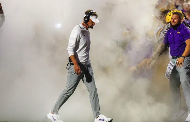 LSU coach Lane Kiffin walks onto the field through smoke before a game at Tiger Stadium
