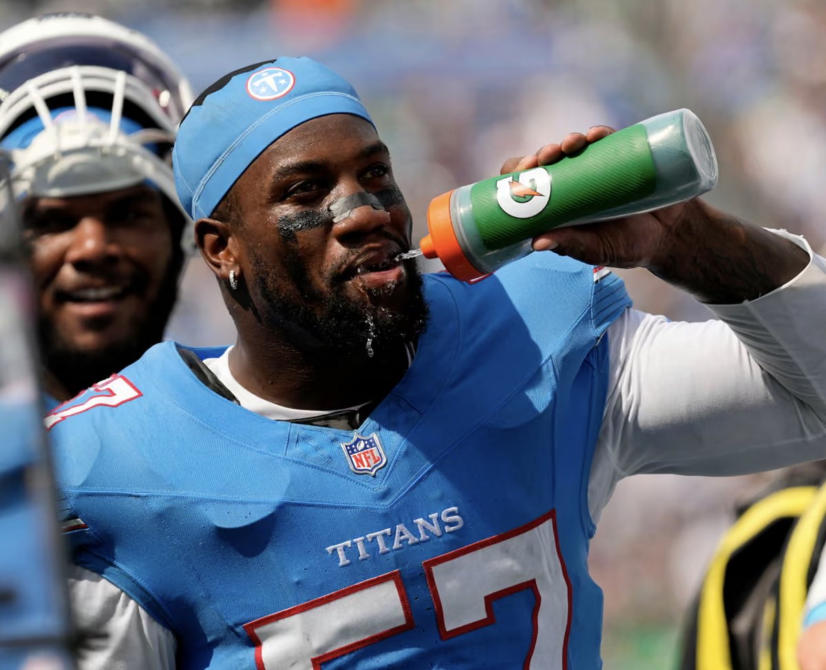 A Tennessee Titans player in a light blue No. 57 jersey drinks from a bottle on the sideline